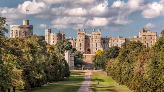 Windsor Castle during golden hour with clouds above and green trees on the grounds